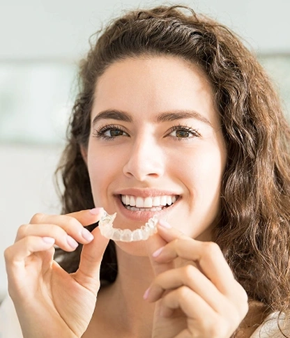 Smiling woman holding an Invisalign clear aligner at Willow Street Dental in Chippewa Falls, WI